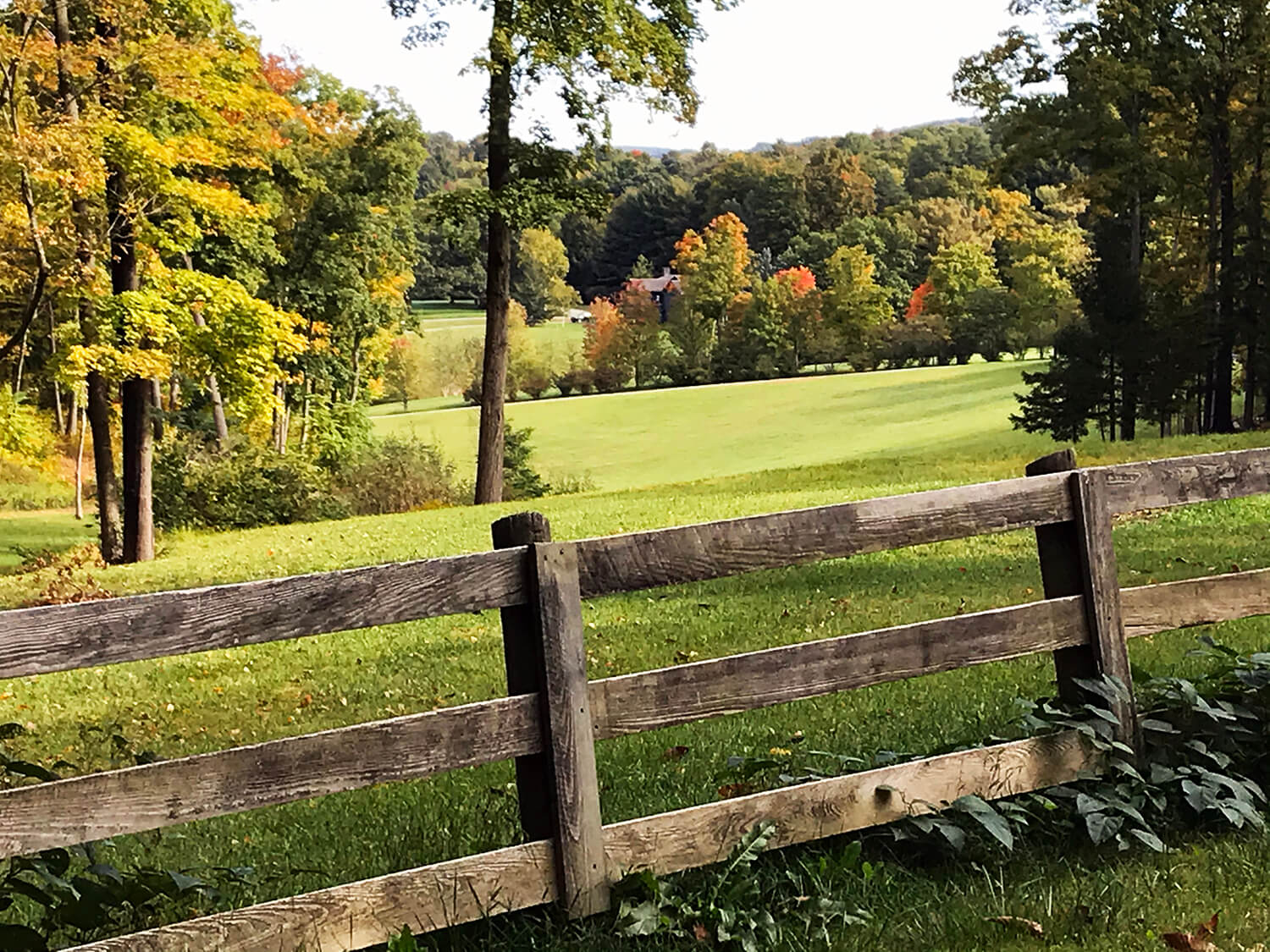 A split rail fence on farmland with distant hills and fall foliage.