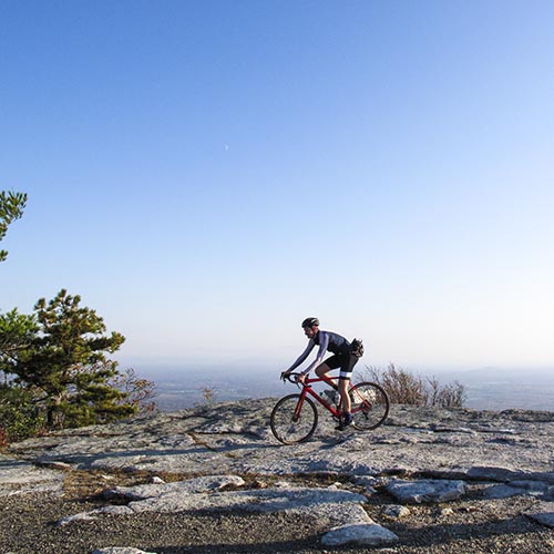 Cyclist on stony cliffside, with wide blue sky in the background