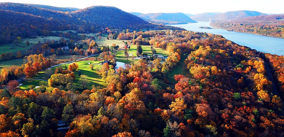 Aerial view of Hudson Highlands in autumn with colorful leaves and the Hudson River in the background.