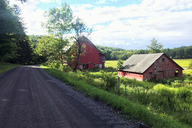 two red barns in a countryside valley under blue skies