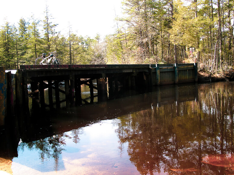 A wooden bridge crosses a stagnant steam