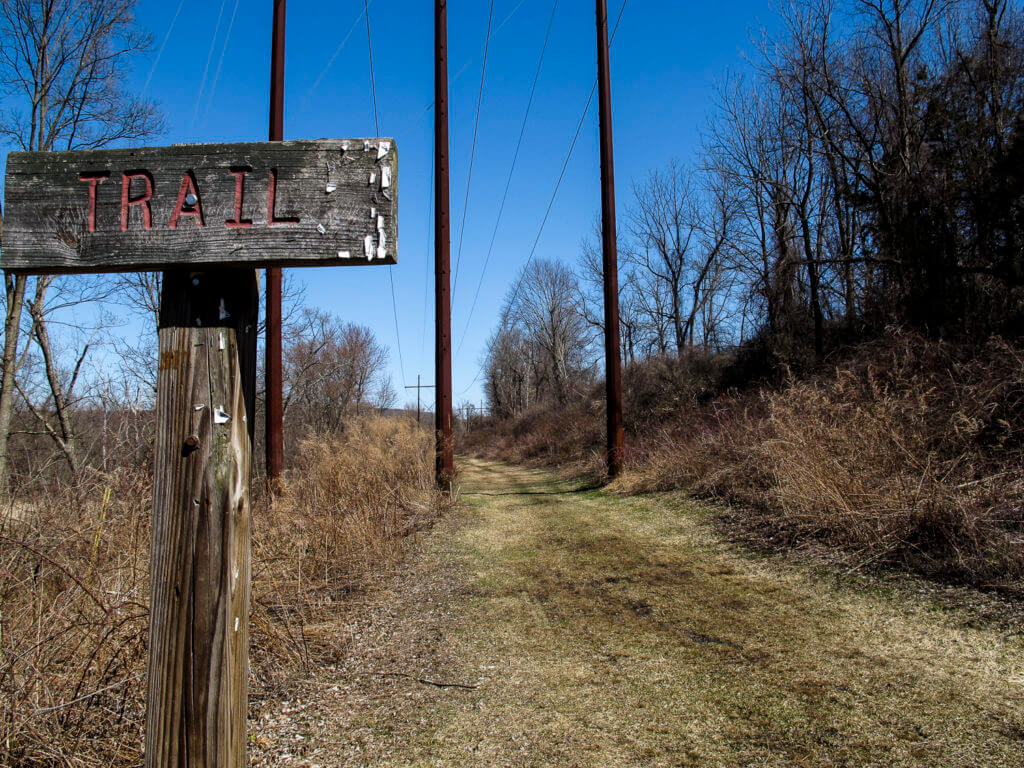 a rustic trail sign and a grassy bike path
